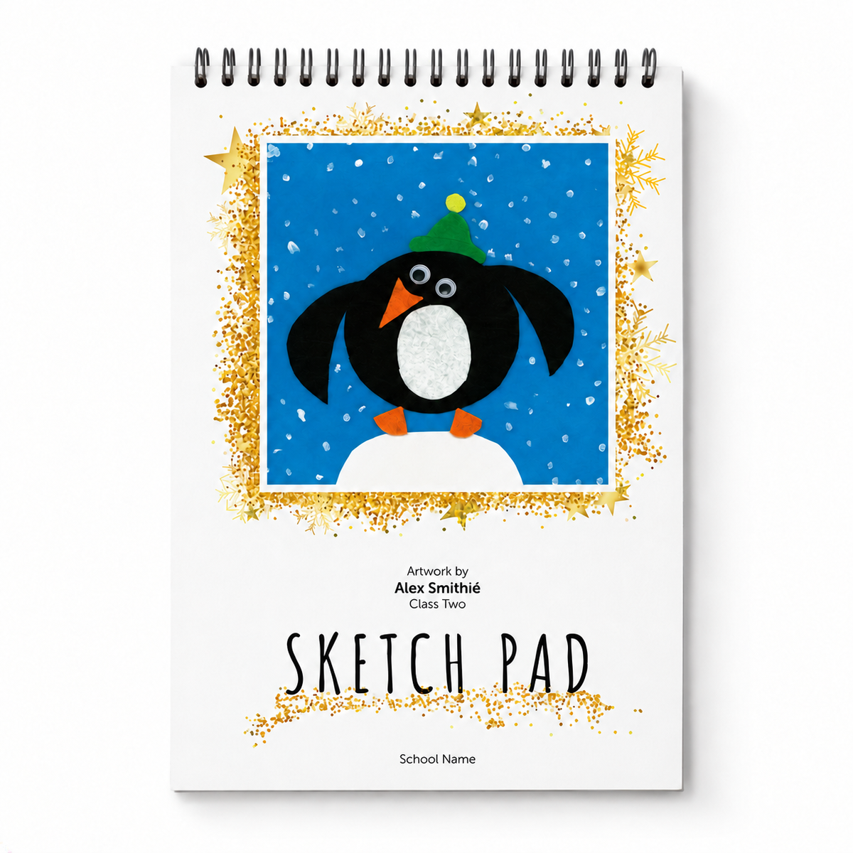 A spiral-bound sketch pad with a white cover, featuring a colorful illustration of a penguin wearing a green hat on a blue snowy background, surrounded by a glittery gold frame. The text 'SKETCH PAD' is printed below the artwork.